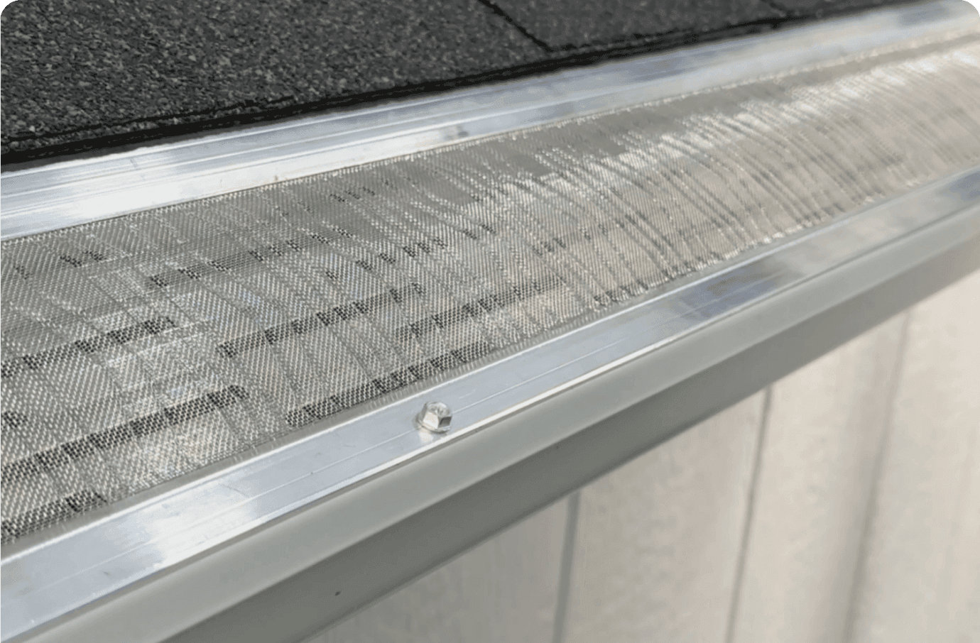 LeafBlaster Pro - Aluminum gutter guard with mesh screen covering the gutter opening, installed along roofline with black shingles visible above