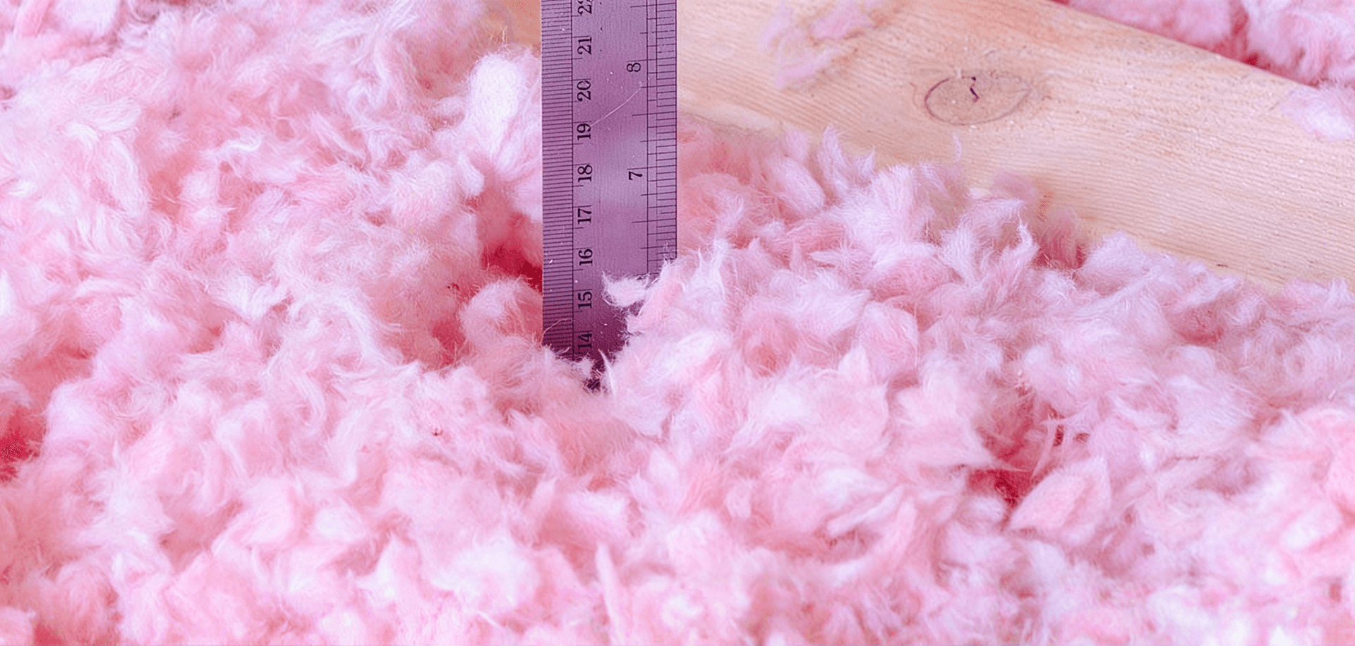 Pink fiberglass insulation with ruler measuring thickness, showing material density and measurement scale
