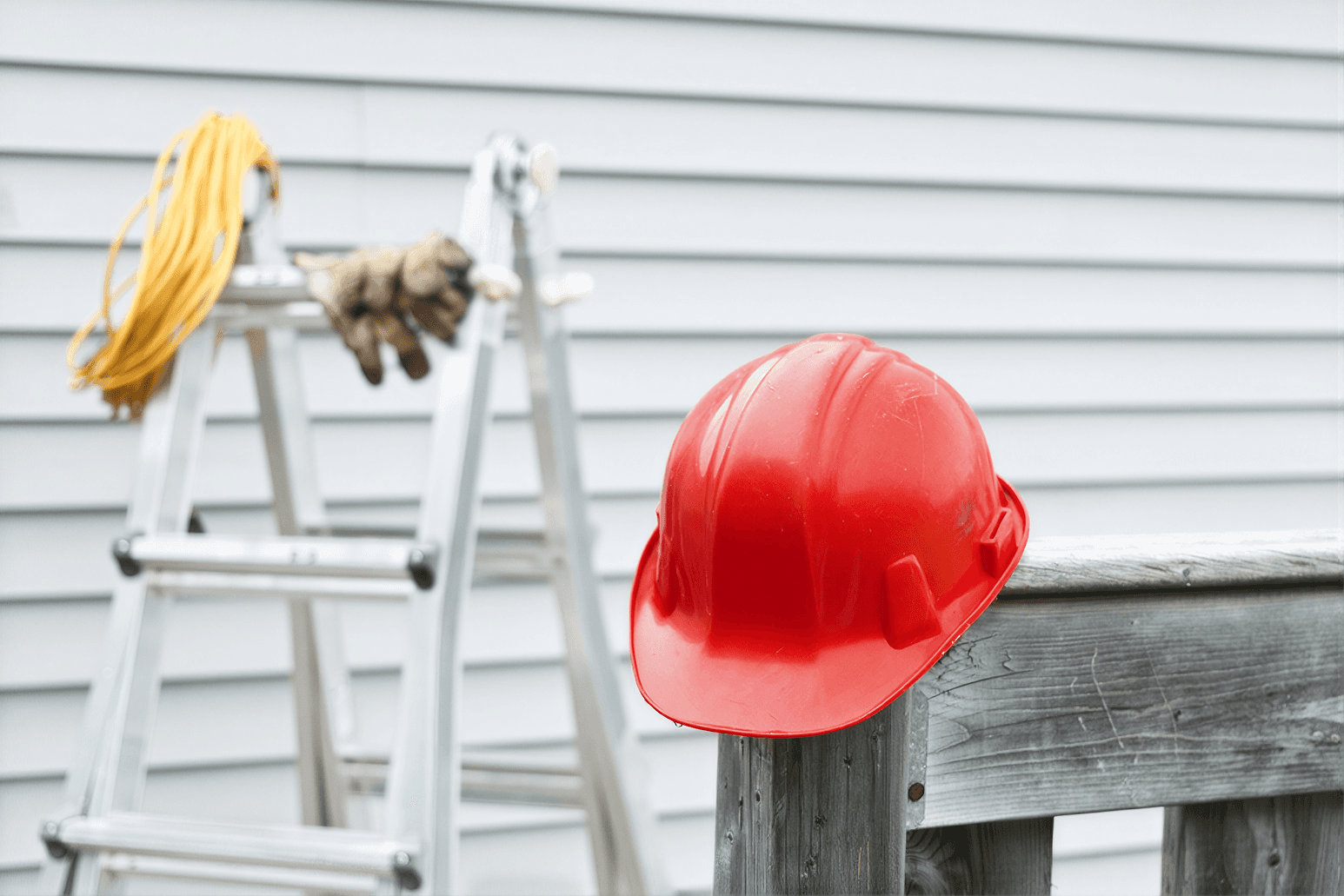 Red hard hat on wooden rail with worker and cat climbing ladder against white house siding