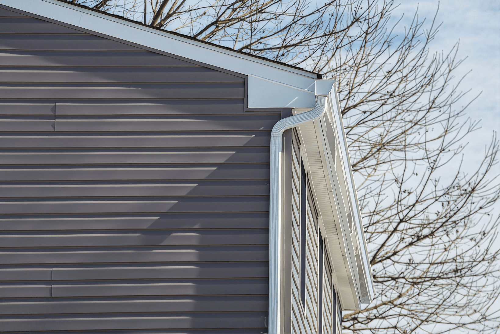 Modern garage with horizontal metal siding and white vertical louvered ventilation system beside bare tree branches