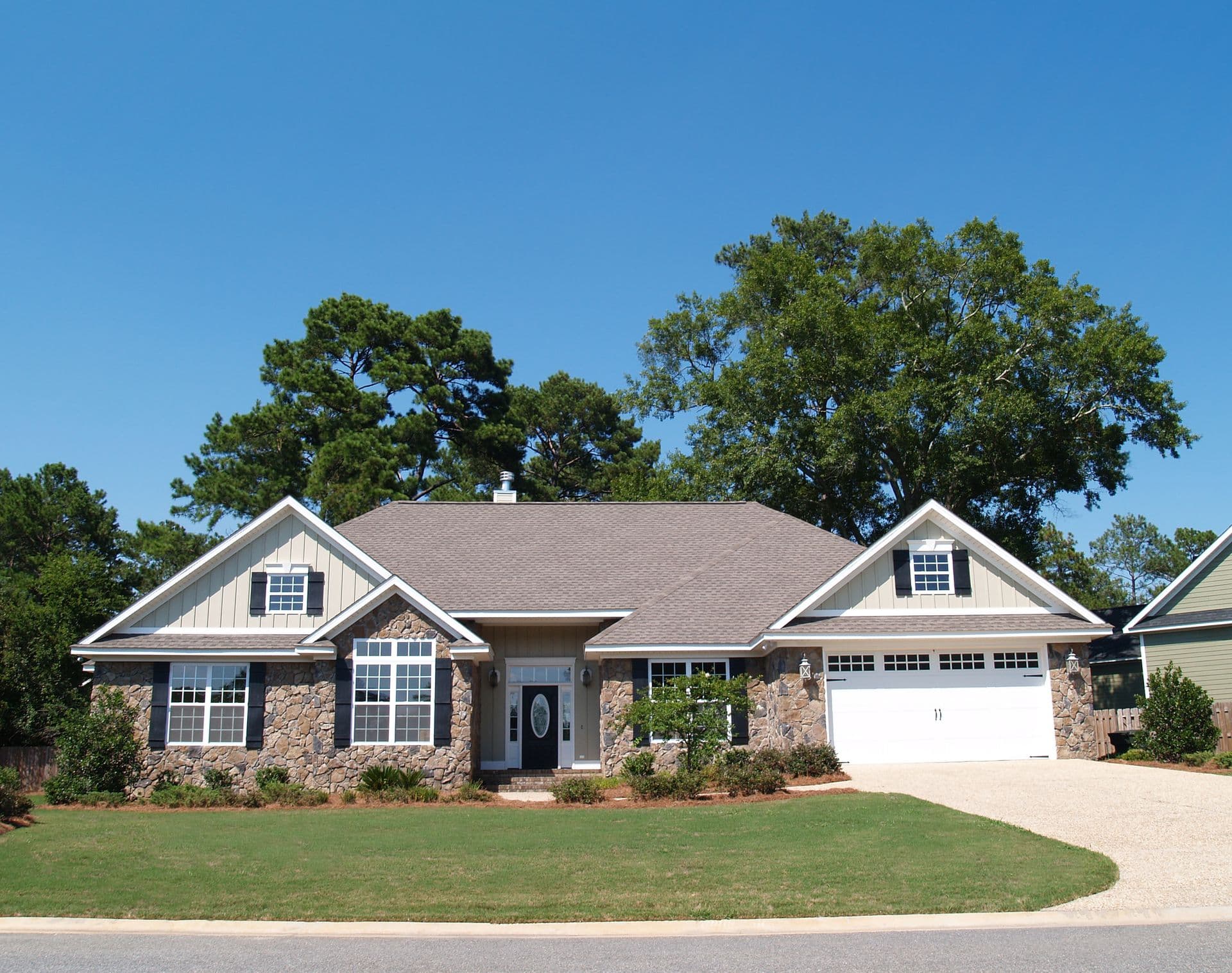Single-story brick home with gray roof, white trim, two-car garage, and manicured lawn surrounded by large shade trees