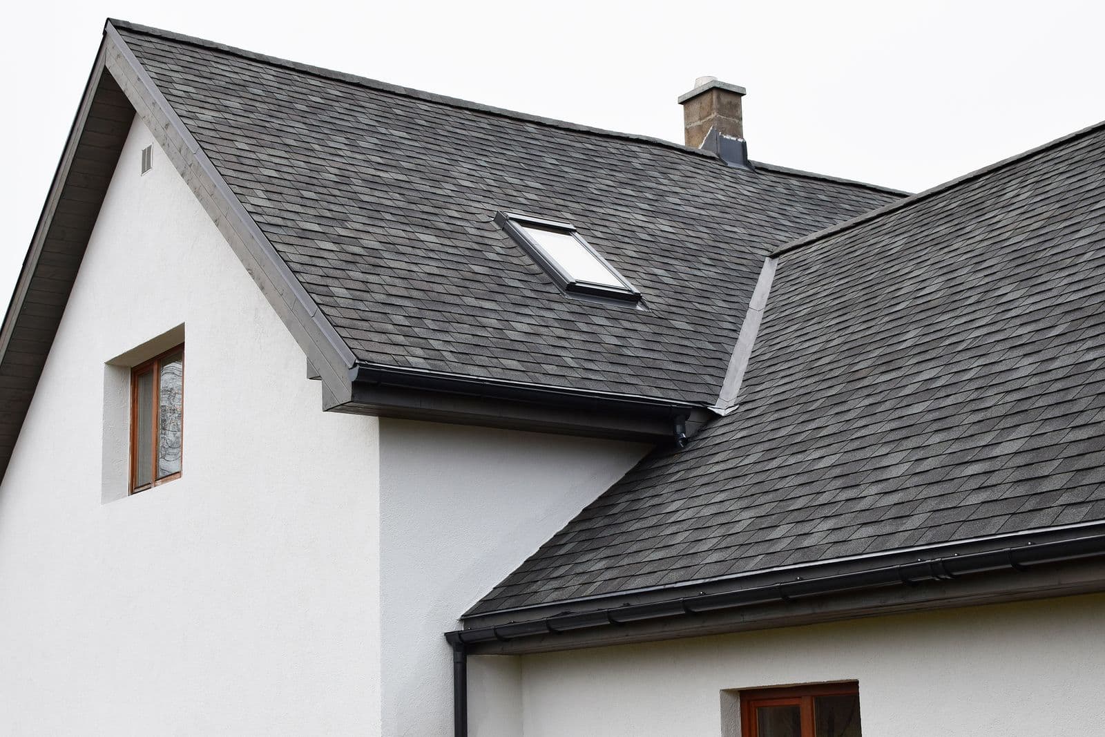 Contemporary white house with dark slate roof, skylight, brick chimney, and wooden-trimmed windows showing modern residential architecture