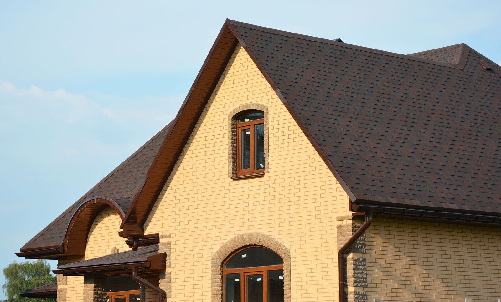 Brick house with peaked roof and dark shingles, featuring arched windows and doors with orange frames