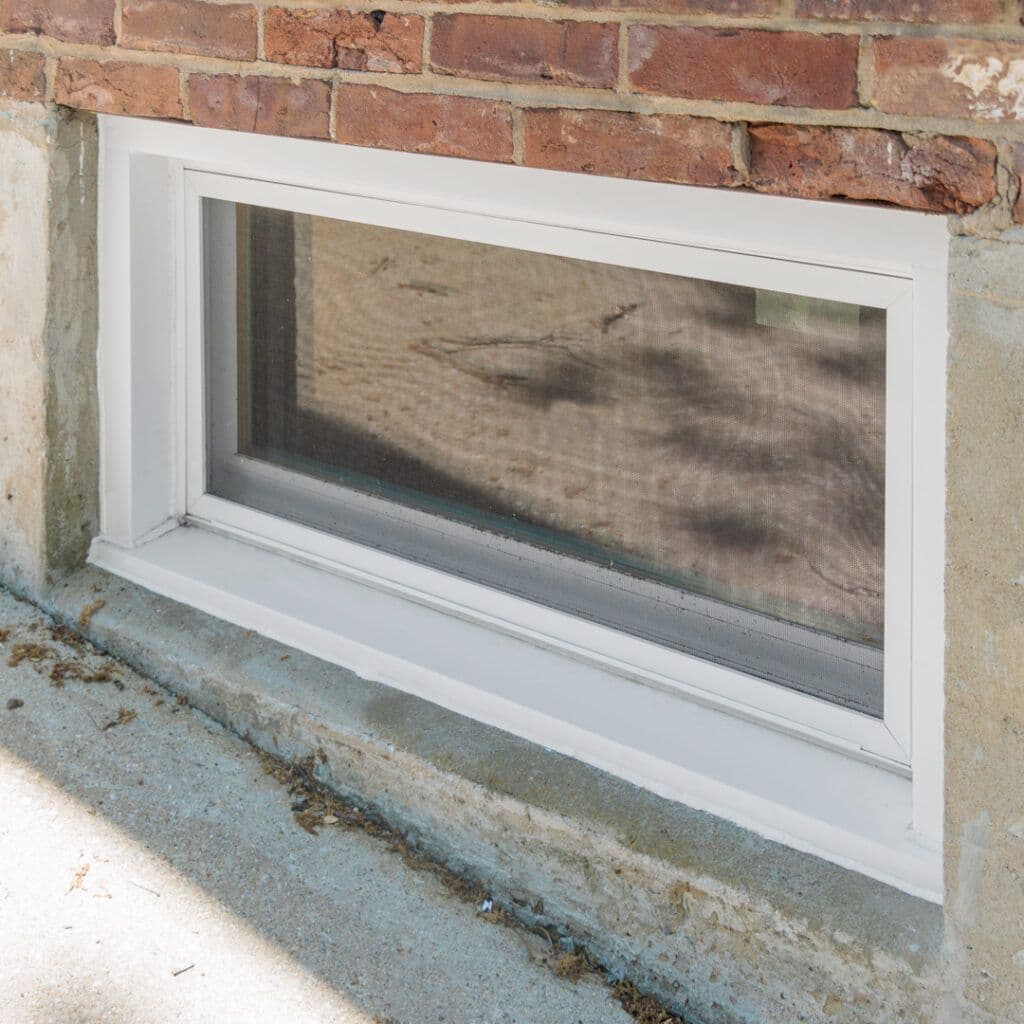 White vinyl basement window with screen installed in brick and concrete foundation wall