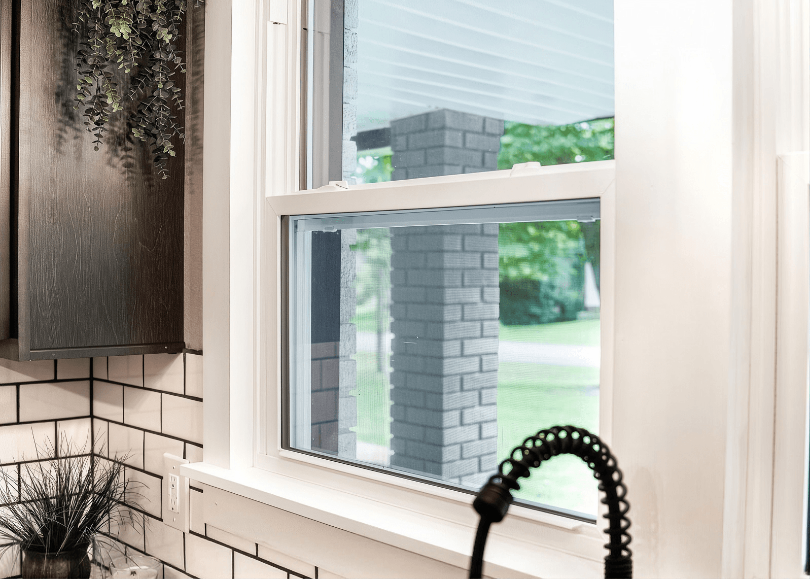 Modern window with sliding glass door and retractable screen, overlooking brick building and green yard, with hanging plant and potted grass on white sill