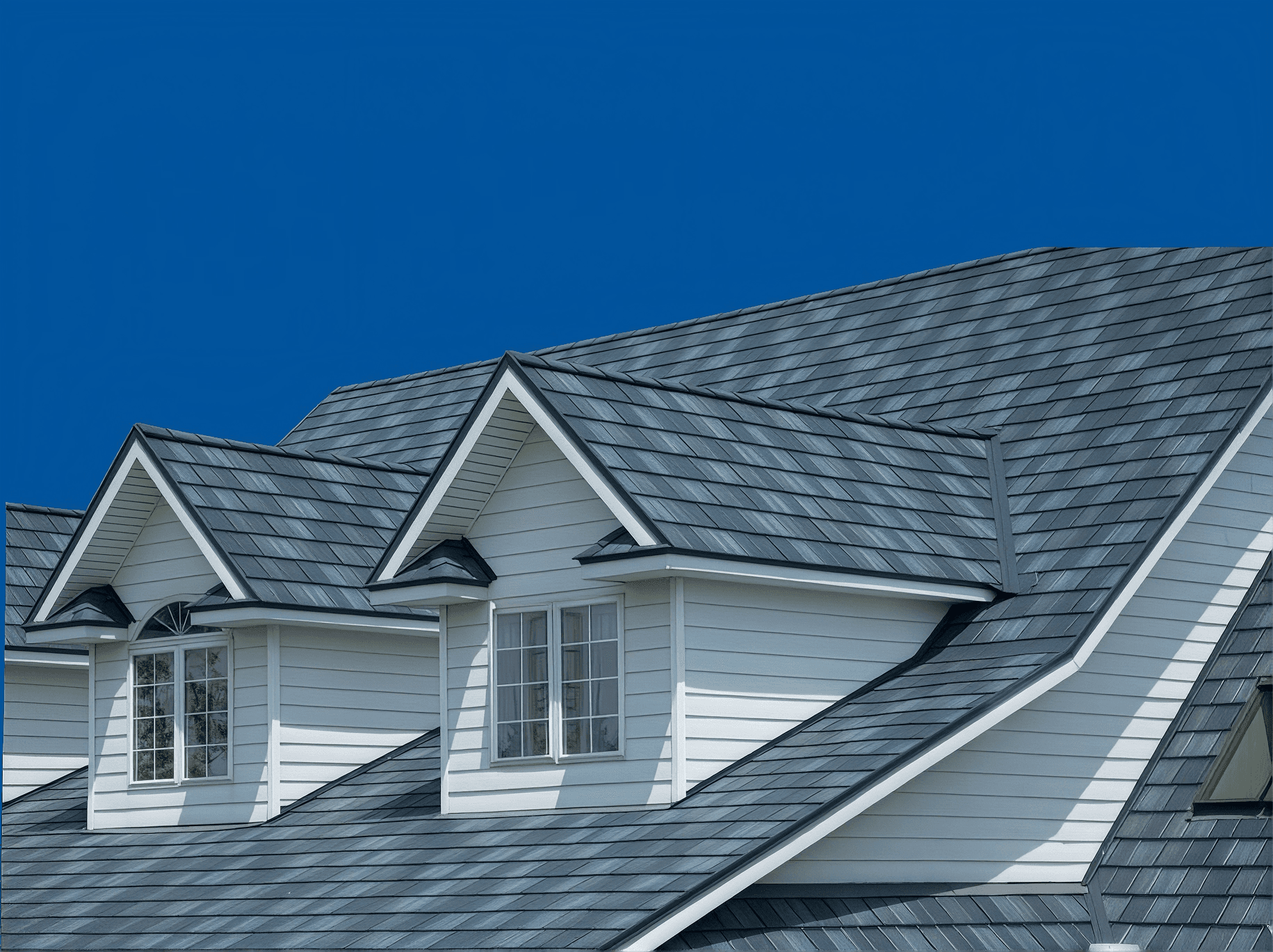 Modern house with white siding and gray metal roof featuring multiple gabled dormers and large windows against clear blue sky