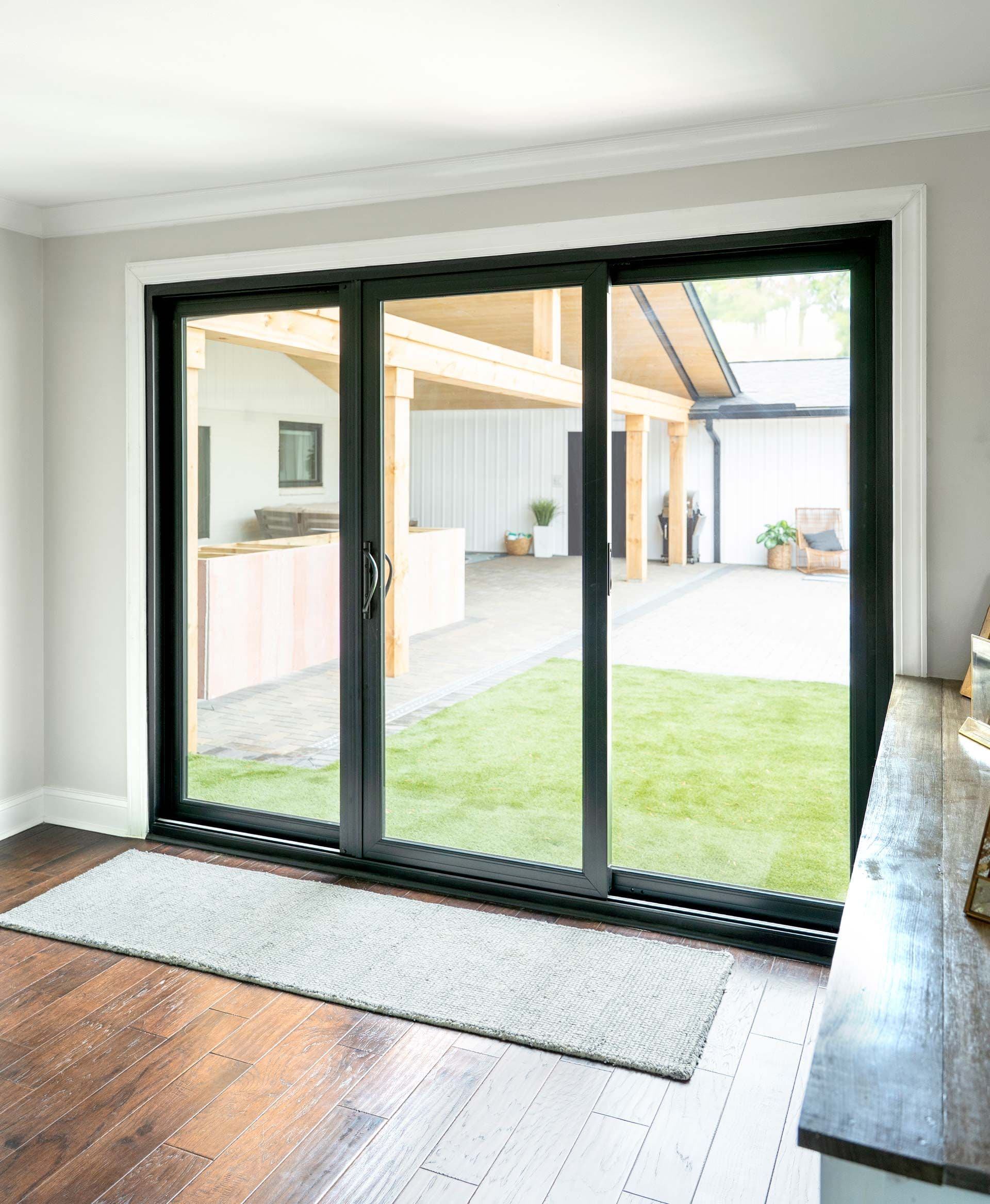 Three-panel black sliding glass doors opening from interior hardwood floor to backyard with green lawn and covered patio area