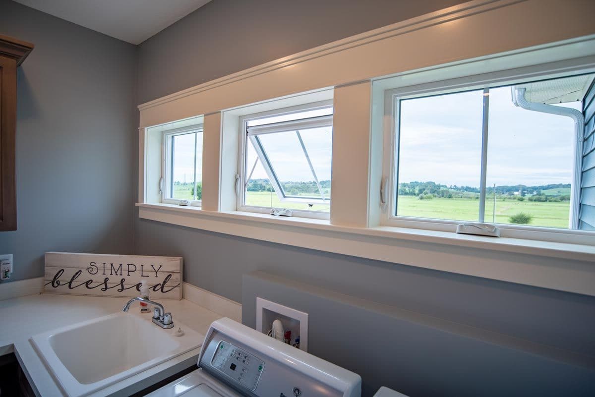 Laundry room with large windows overlooking rural farmland, white sink and washer, and simply blessed wooden sign on wall