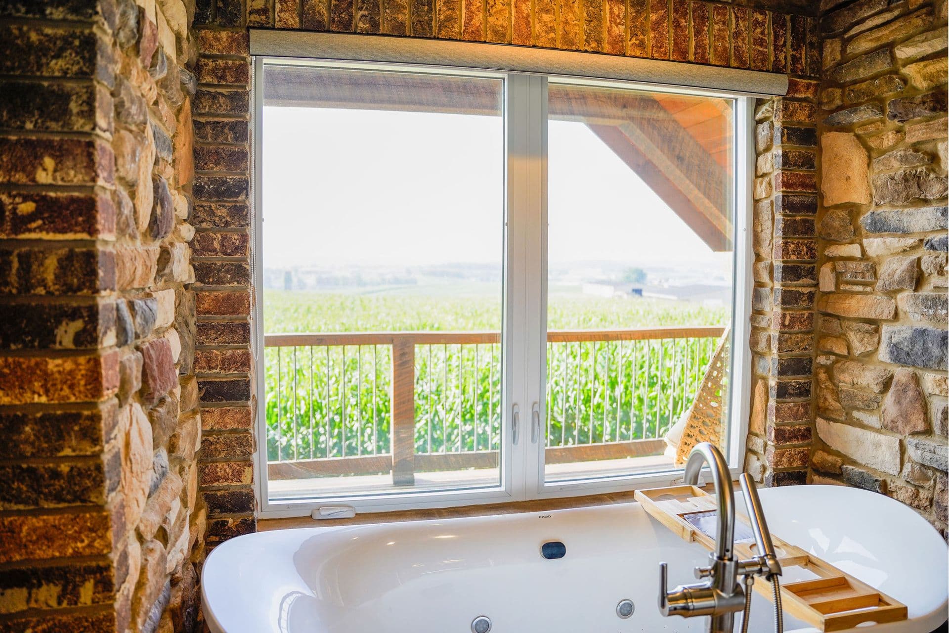 Bathroom with white soaking tub overlooking sliding glass doors framing agricultural fields and countryside landscape beyond
