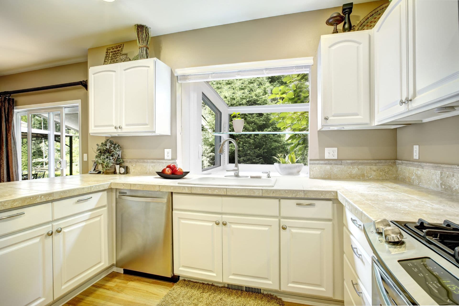 Bright kitchen with cream-colored cabinets, granite countertops, stainless steel appliances, and a large window overlooking green foliage above the sink