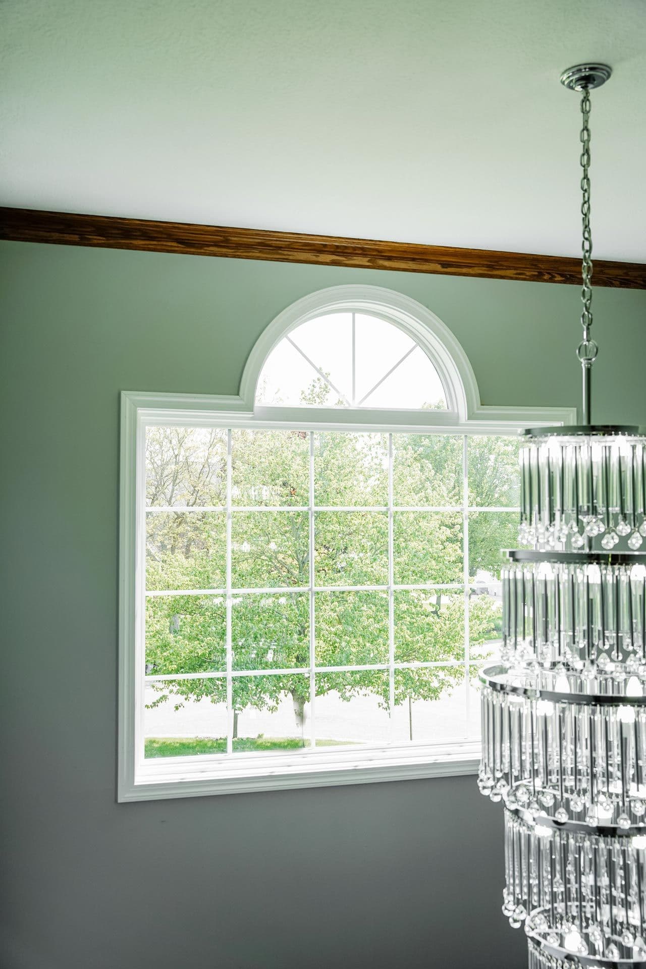 Bright room with sage green walls, large multi-pane window overlooking green trees, and a crystal chandelier hanging from the ceiling