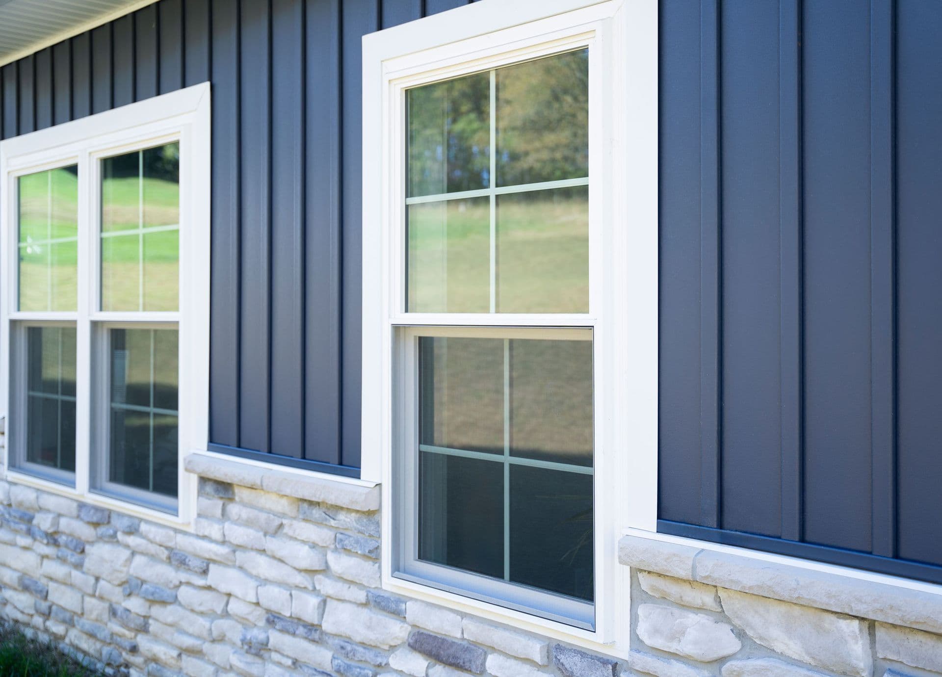 White-framed windows on blue corrugated metal siding above stone foundation, showing green landscape and trees through glass panes