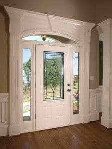 White front entryway with double doors, sidelights, and arched transom window with decorative grille, leading to outdoor view