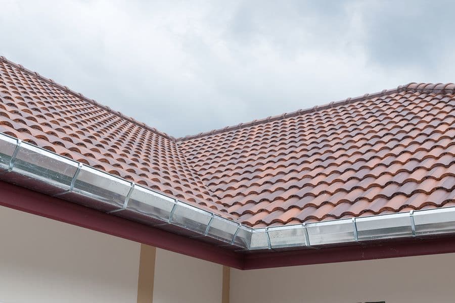 Pitched roof with terra cotta clay tiles and aluminum gutters against cloudy sky