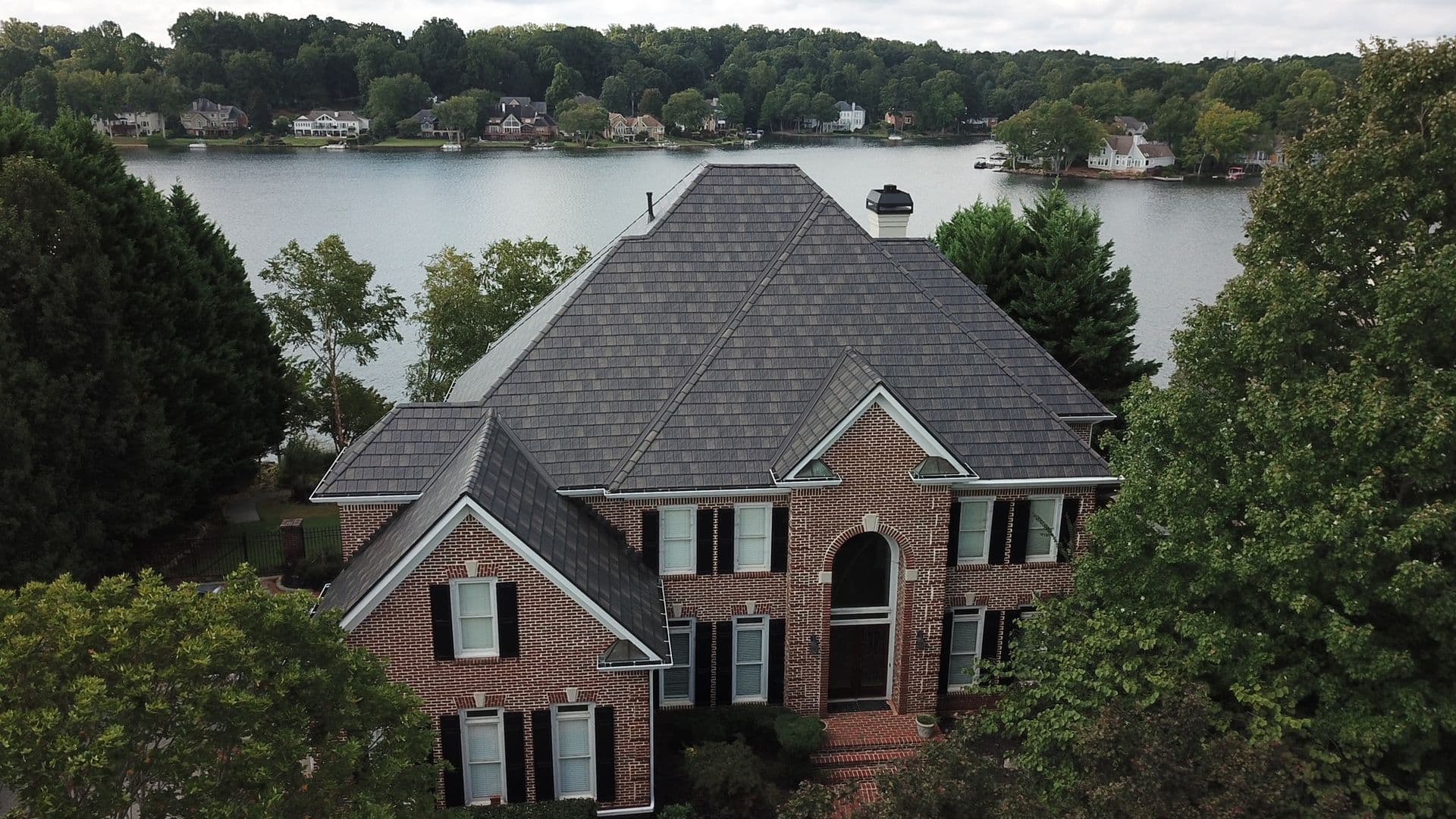 Aerial view of a brick residential home with slate roof overlooking a waterfront neighborhood with docked boats and tree-lined streets