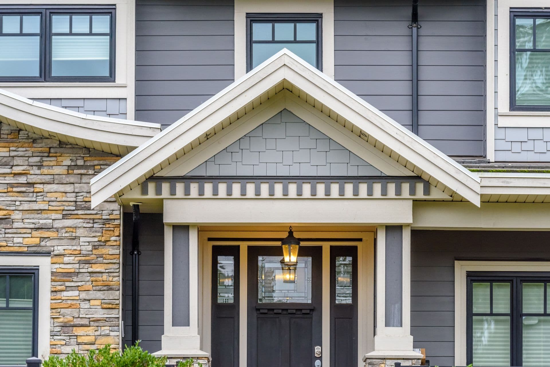 Modern home facade with black front door, white gabled entryway, stone accent wall, and mixed material siding including gray horizontal boards and light blue shingles