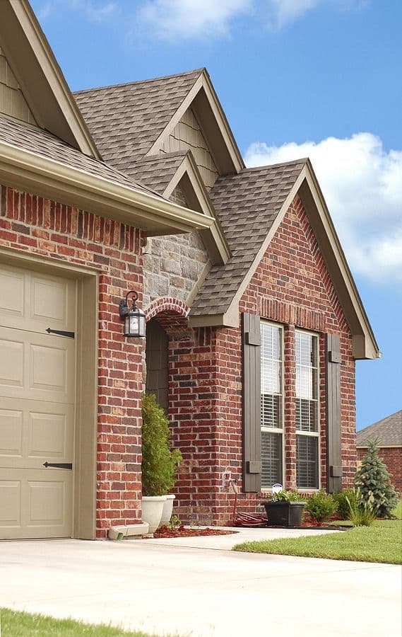 Traditional two-story brick home with garage, peaked roof, and front landscaping under clear blue sky