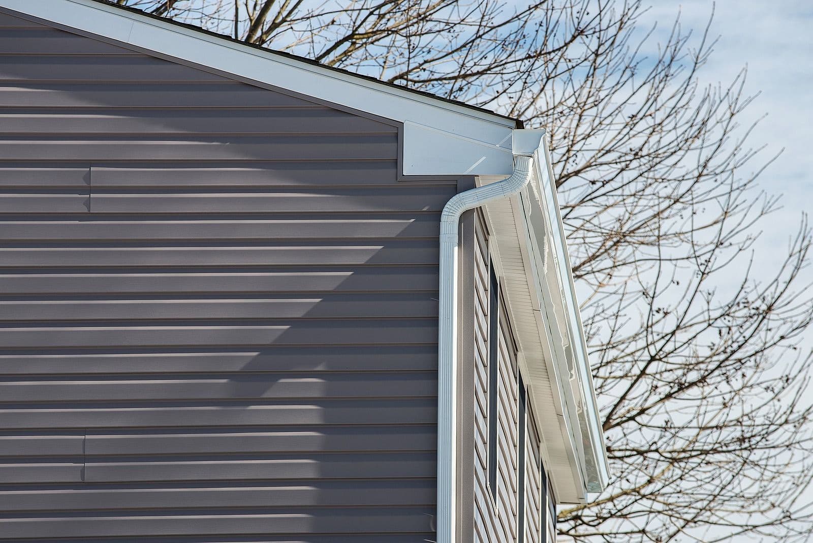 Modern house exterior showing gray metal siding, white trim, and louvered vent detail against bare tree branches and blue sky