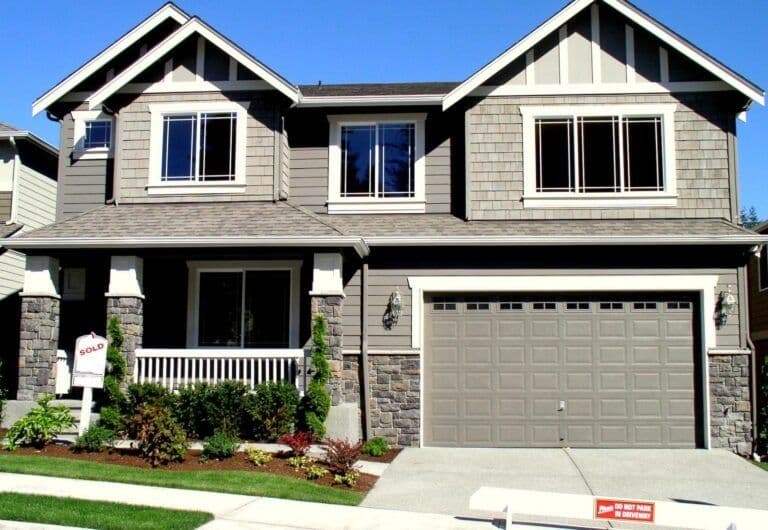 Two-story suburban home with mixed siding, front porch, and attached garage, with "Sold" real estate sign visible