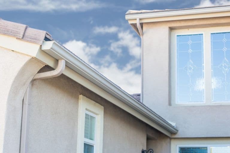 Exterior view of residential home showing white gutters and downspout along roof edge with windows visible