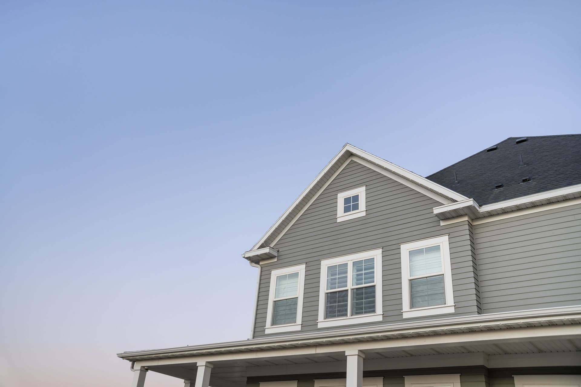 Two-story house with gray siding, white trim, and black roof against clear blue sky