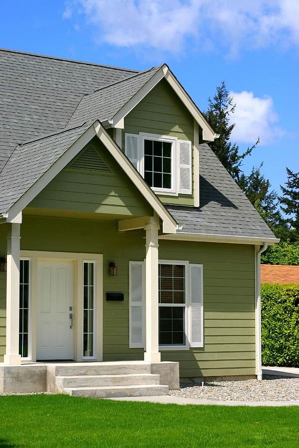 Green and white cottage-style house with peaked roof, dormer window, front porch, and landscaped lawn