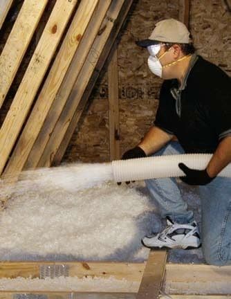 Worker installing insulation batts between wooden wall studs in home construction