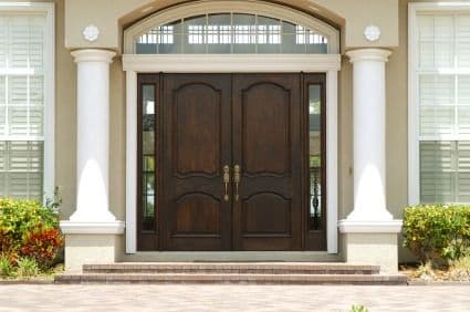 Elegant dark wood double entry doors with arched transom window, flanked by white columns and potted plants on a brick porch