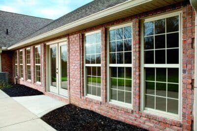 Brick home exterior with multiple large windows and glass doors along the front, mulch landscaping, and concrete patio area