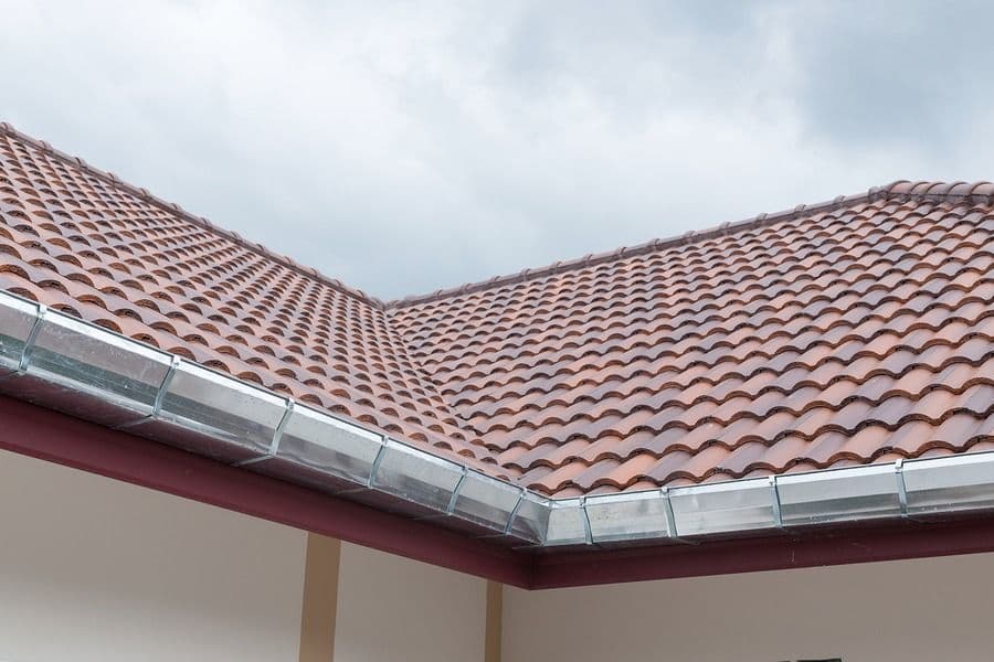 Terracotta clay tile roof with metal gutters and downspouts against cloudy sky