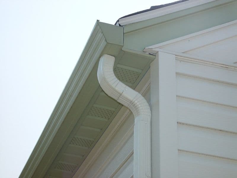 White downspout attached to house gutter system, directing rainwater away from the building foundation
