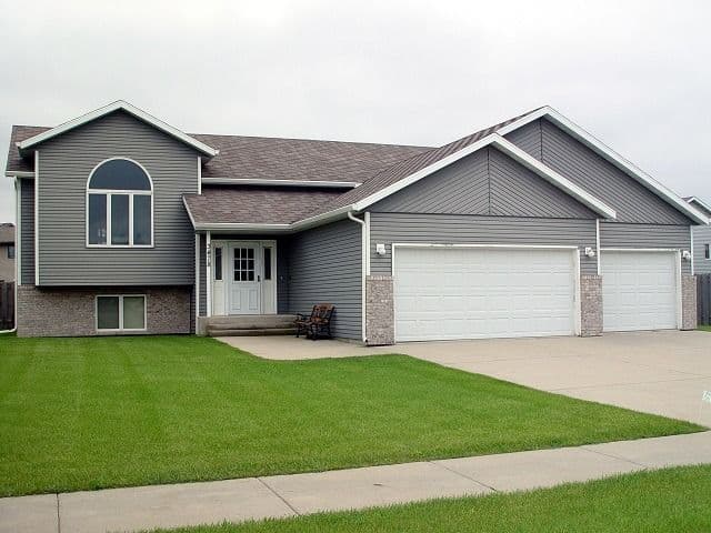 Single-story gray and brick residential home with front-loading two-car garage, arched window, and manicured lawn