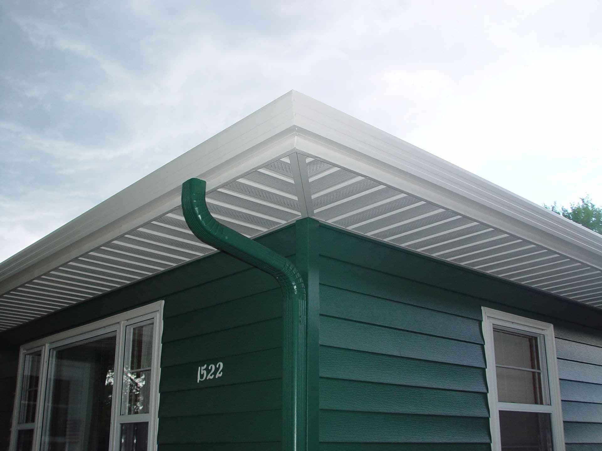 Green house exterior with address 1522, white-trimmed windows and doors, and white metal pergola roof structure with horizontal slats