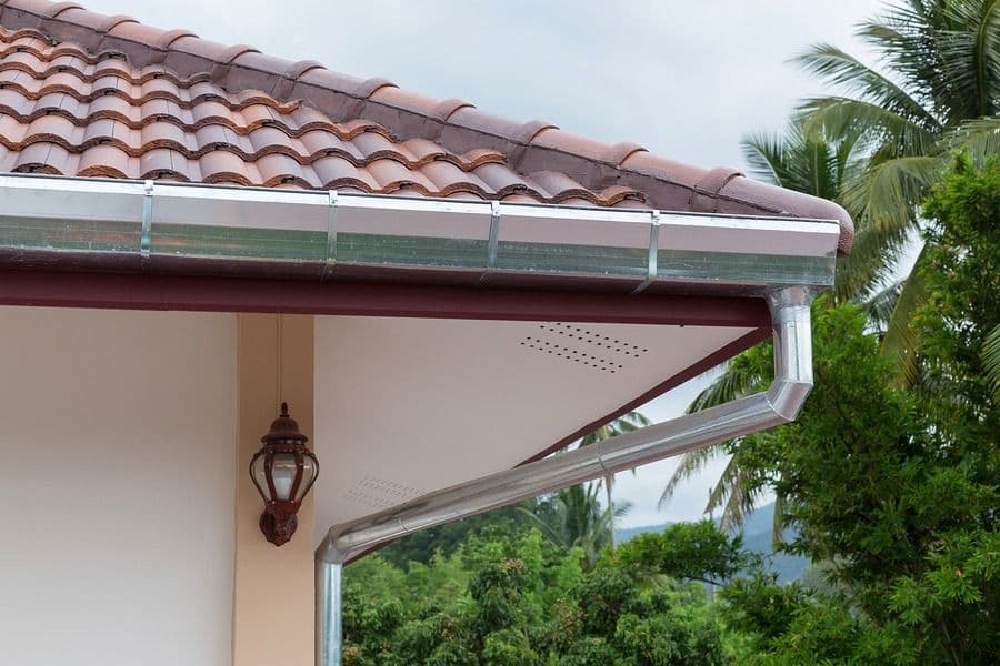 Gutter guard installed on roof edge with clay tile roofing and palm trees visible in background