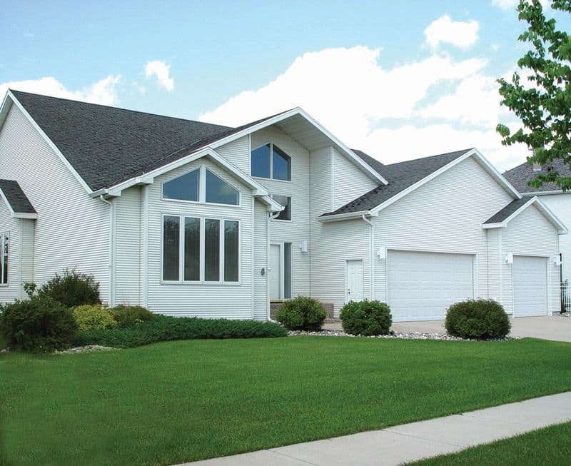 Modern two-story white house with attached two-car garage, landscaped front lawn, and dark roof shingles