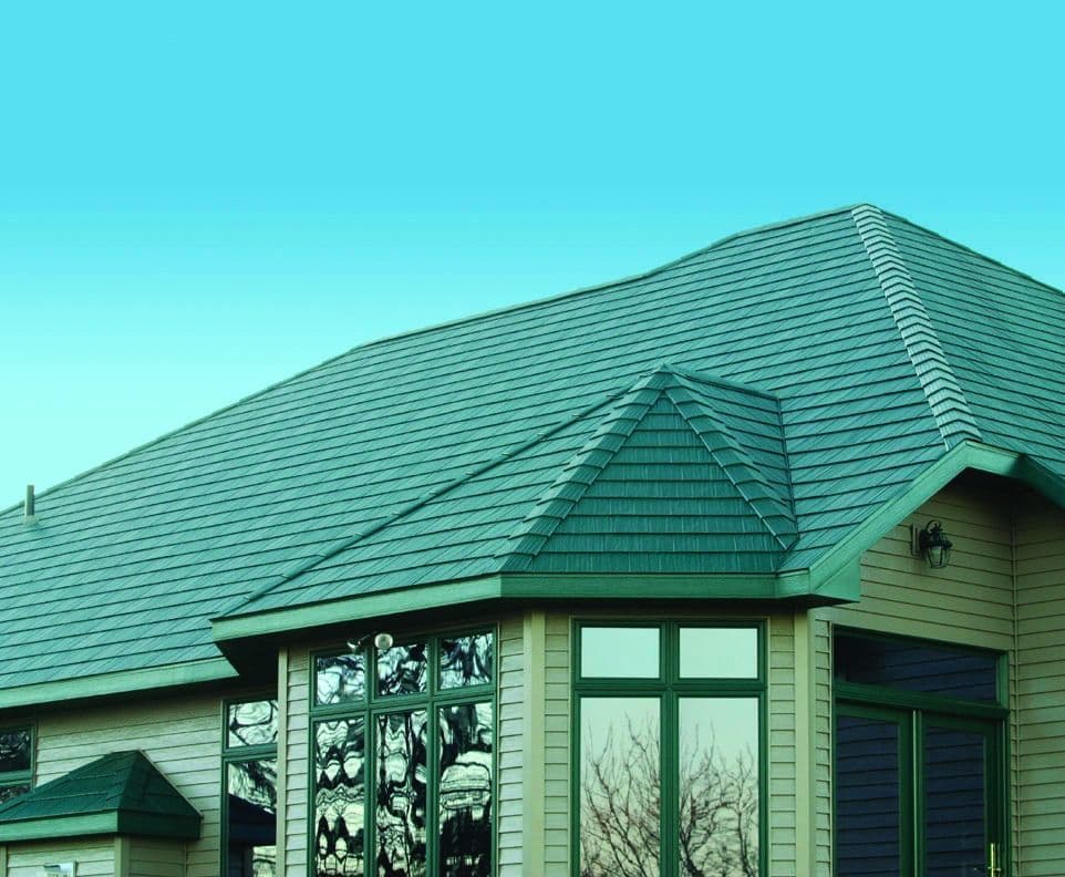 House exterior featuring an angled metal roof with green shingles and a peaked turret section, complemented by green siding and large multi-pane windows