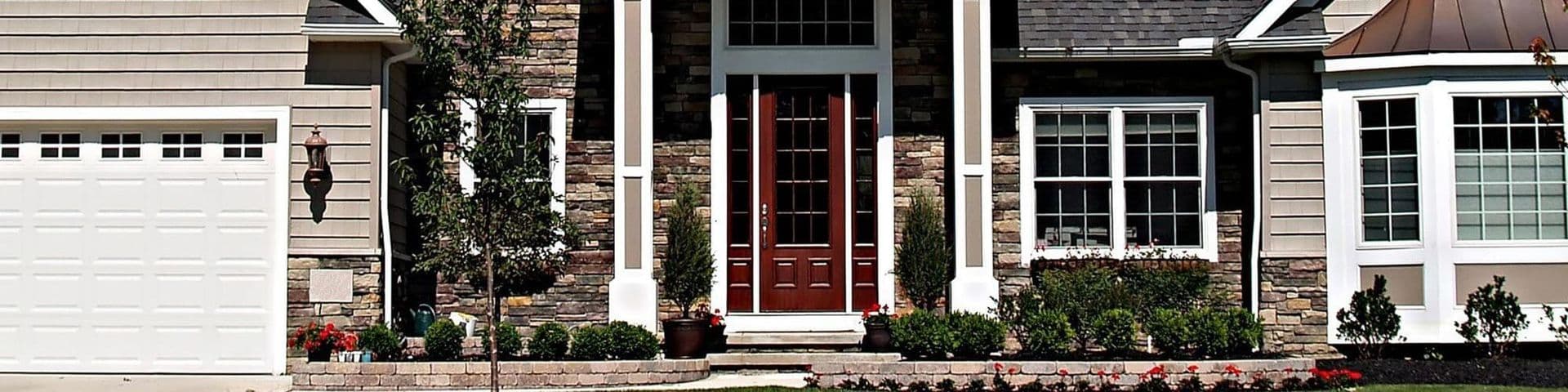 Front exterior of contemporary home with red double doors, stone facade, white garage door on left, and white-trimmed windows with landscaping