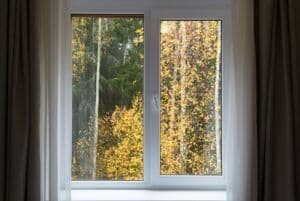 Window with brown curtains showing autumn trees with golden and green foliage outside