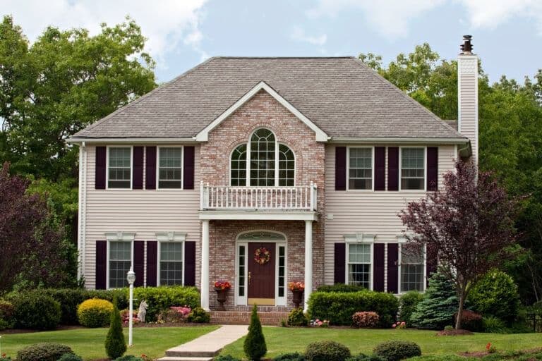Two-story brick and siding house with dark shutters, arched window, front porch, and manicured landscaping