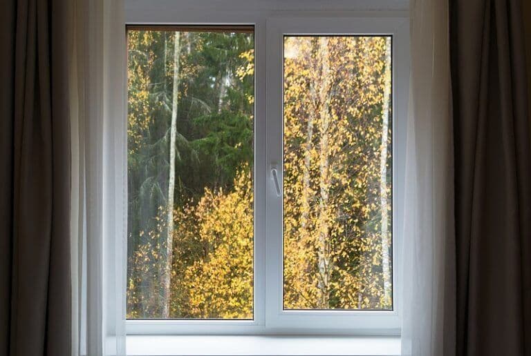 Two tall windows with white frames showing a forest view with birch trees and golden autumn foliage, flanked by brown curtains