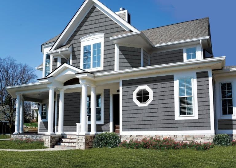 Two-story gray and white house with covered front porch, white columns, gabled roof, and manicured landscaping under clear blue sky grey pillar