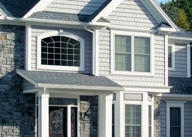 Two-story white house with stone accents, arched window above the front door, and multiple windows on the facade