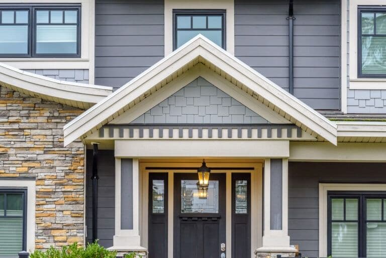 Modern home front entrance with peaked gable roof, black double doors, white columns, brass lantern fixture, and mixed stone and shingle exterior materials