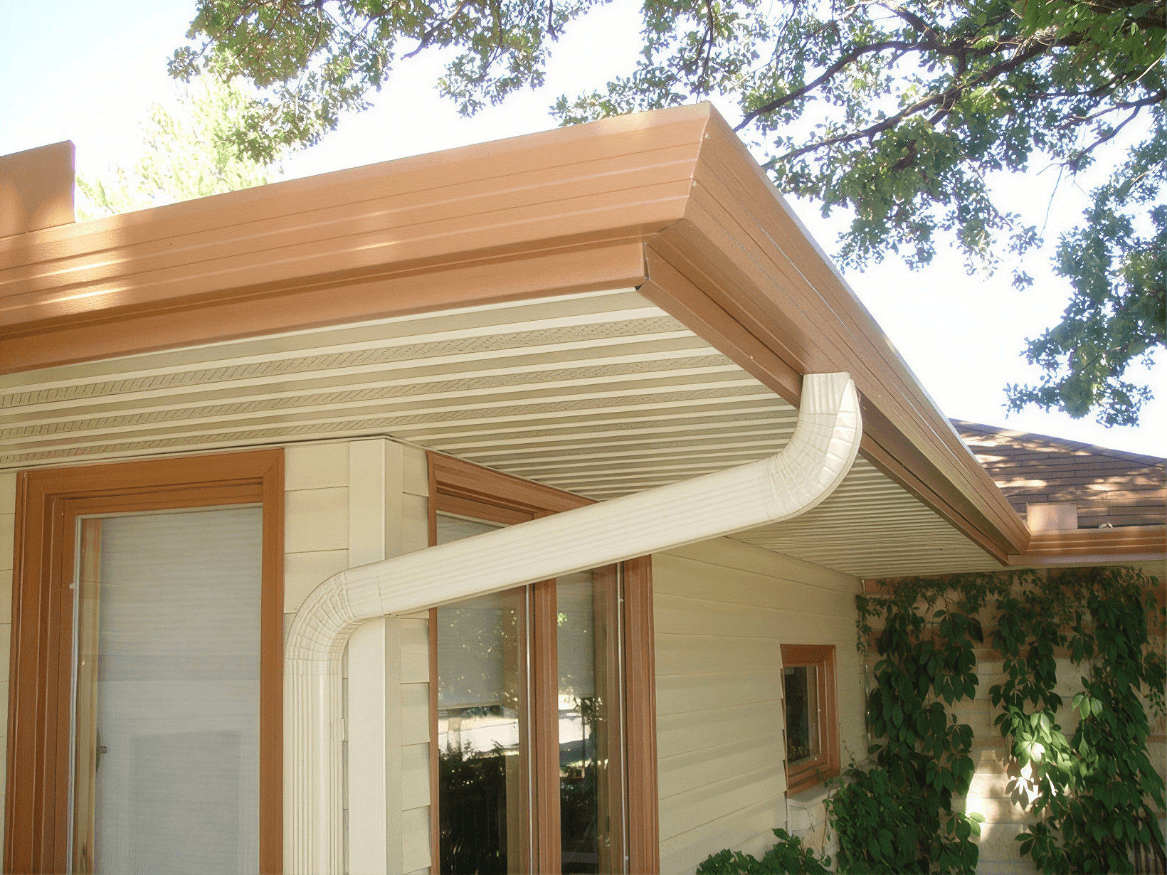 Modern home exterior with cream and wood-toned fascia, gutters, and soffit under large overhanging tree branches