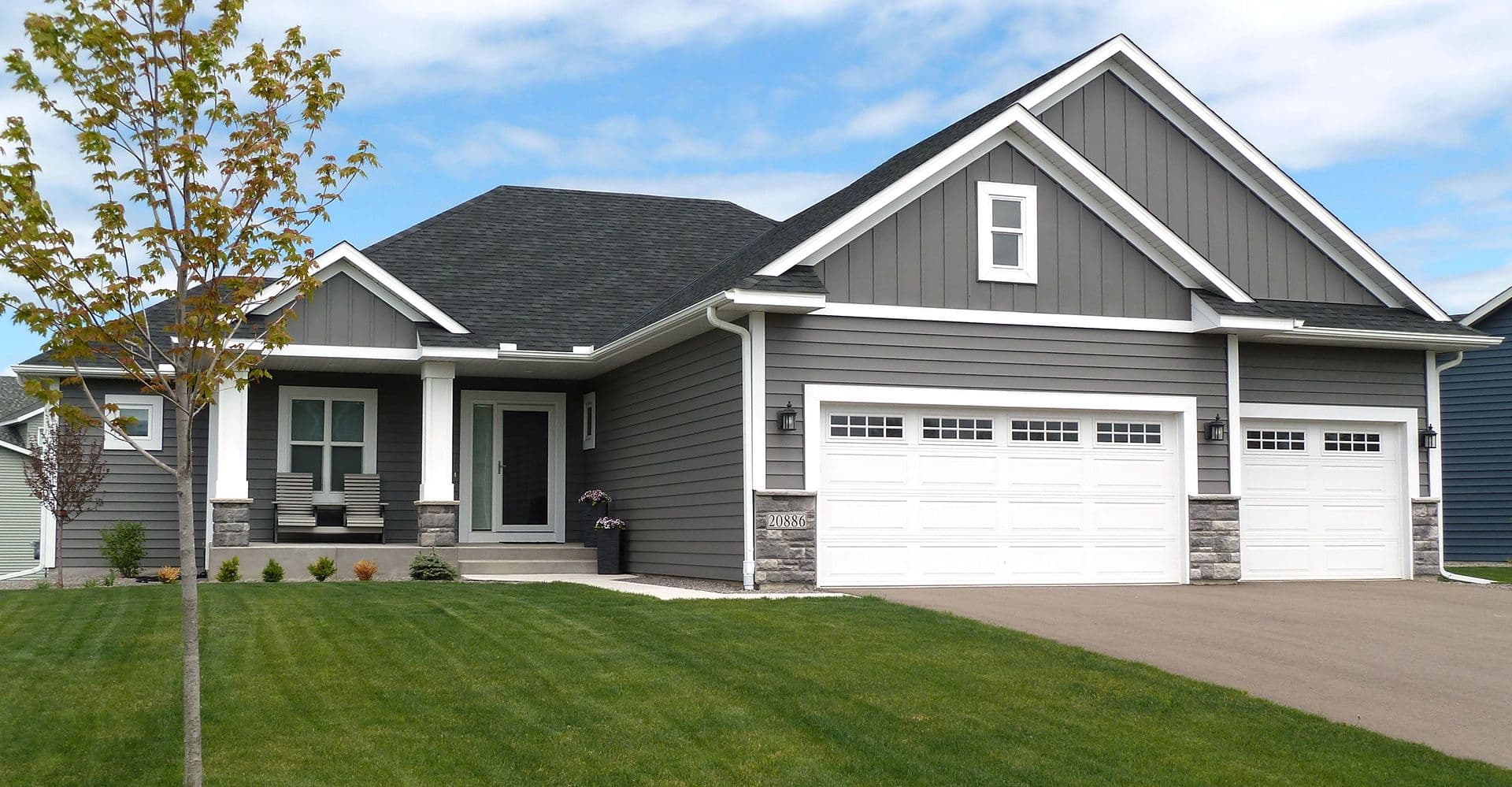 Modern gray and white single-story home with covered front porch, two-car garage, and manicured lawn on a clear day