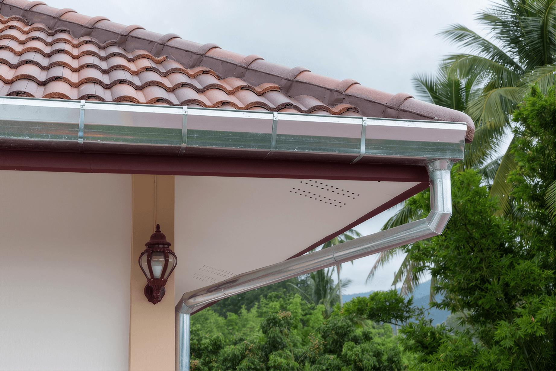 Gutter guard system installed along terra cotta tile roof edge with metal fascia and aluminum gutters, palm trees visible in background