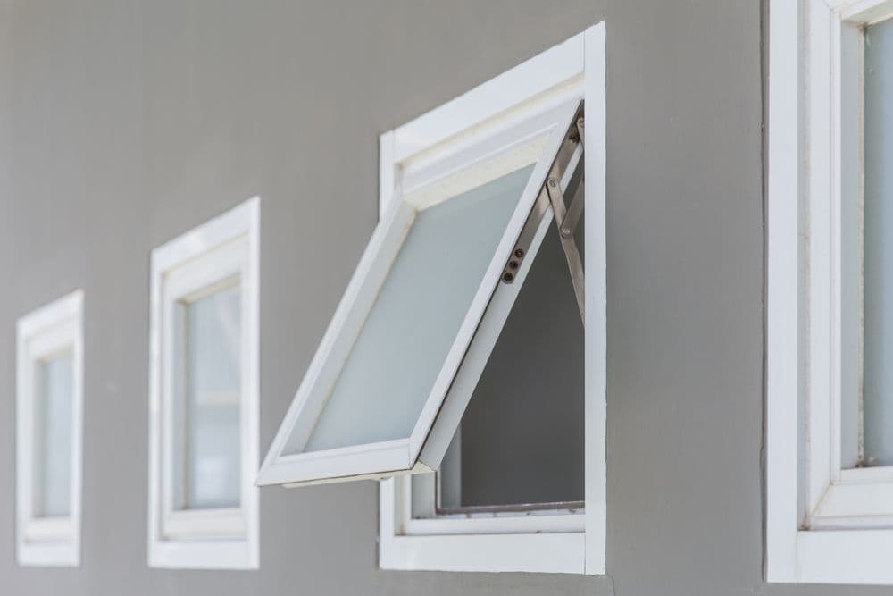 Awning-style window with white frame propped open against gray wall, flanked by two closed windows