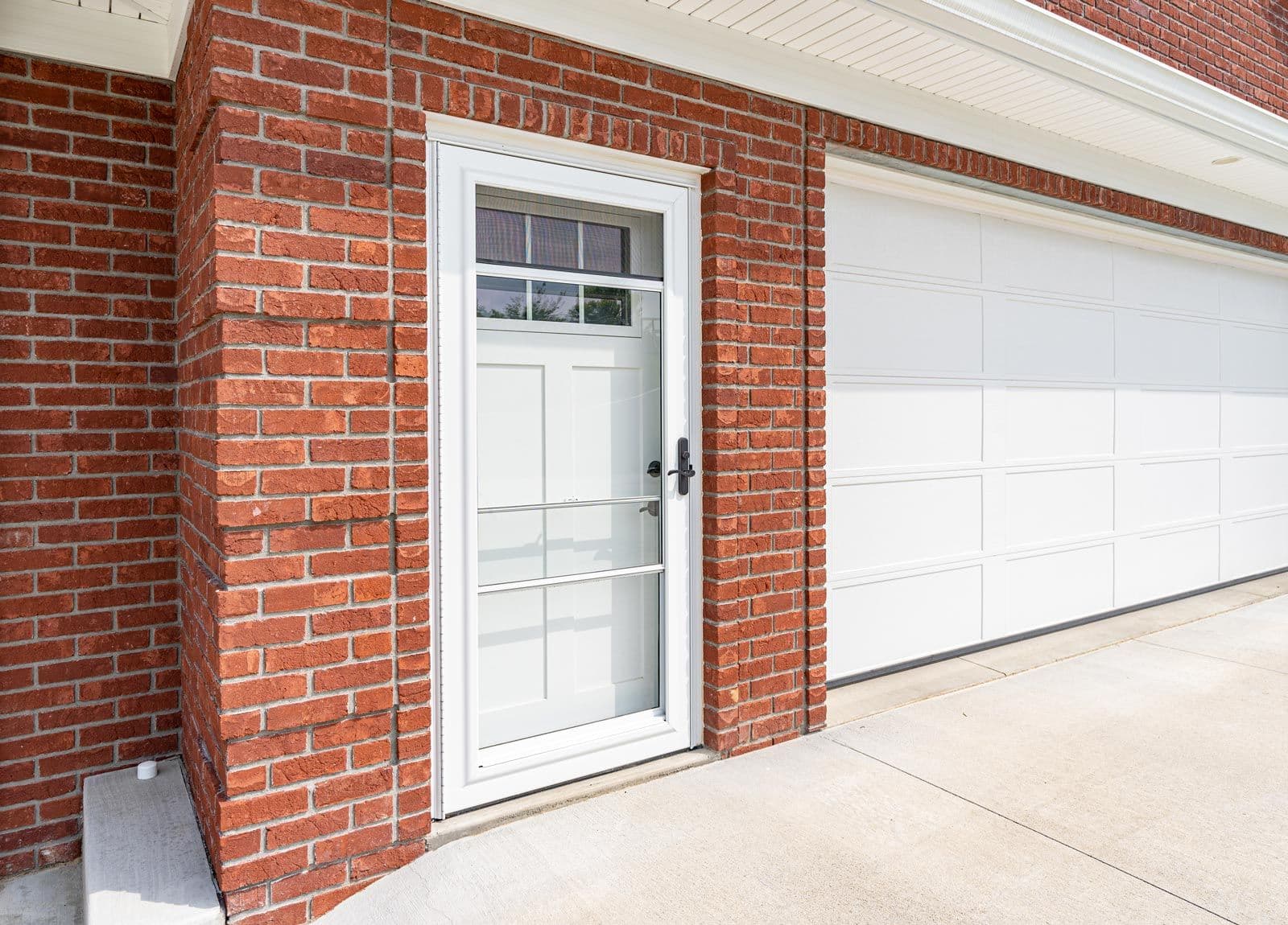 Brick garage exterior with white-framed glass entry door and white overhead garage door