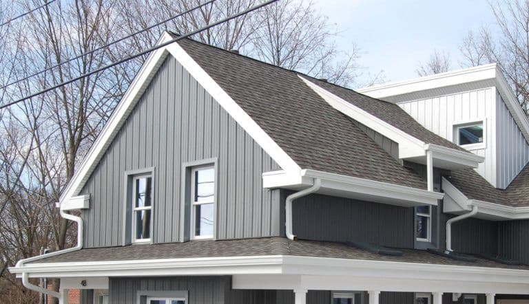 Modern two-story farmhouse with gray metal siding, white trim, two-car garage, and dark gray roof against bare winter trees