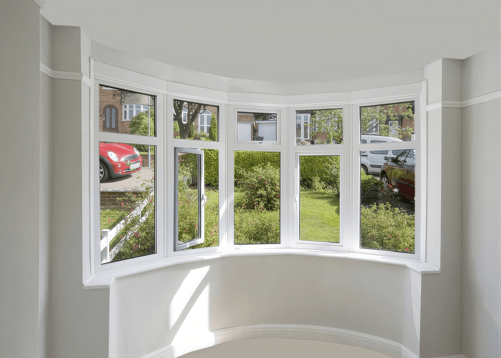 Bay window with white frames overlooking garden and driveway with parked cars